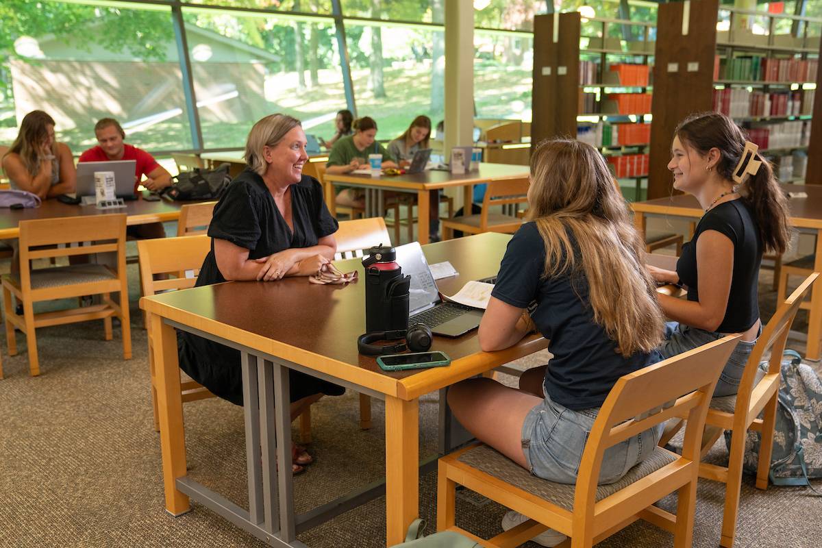 Students and Student Success Director Sara Haviland talk in the library at a table