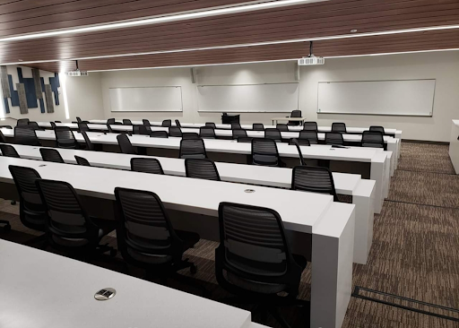 A lecture hall in Albertus Magnus Science Building with long white tables lined with swivel computer chairs, tiered with the highest level in the back, all facing the whiteboards at the low front of the room.