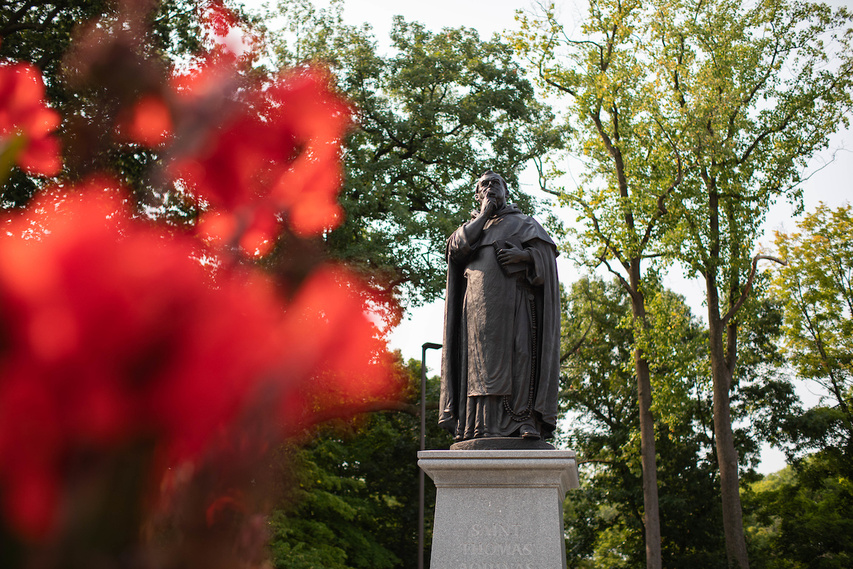 Sculpture of Saint Thomas Aquinas with red flowers in the foreground