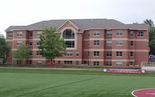 St. Rose of Lima Hall as viewed from the Soccer field. Red brick building with four stories and a large arched window in the center.