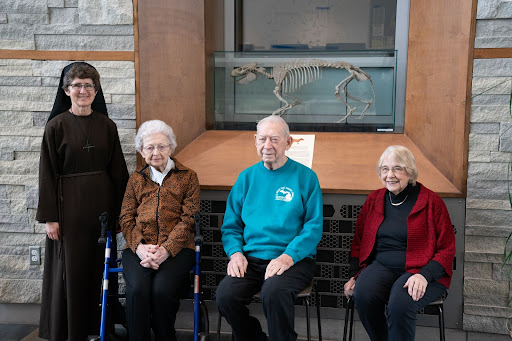 Ted Thompson with his wife Rita, Sister Damien Savino, and Sister Aquinas in front of the Oreodont skeleton displayed in Albertus Magnus Hall