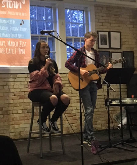 two students on stage singing and playing the guitar