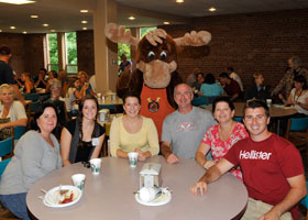 people sitting around a table in the cafeteria with a moose mascot