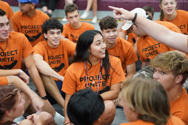 Students in matching shirts sitting on the ground wearing AQ lanyards