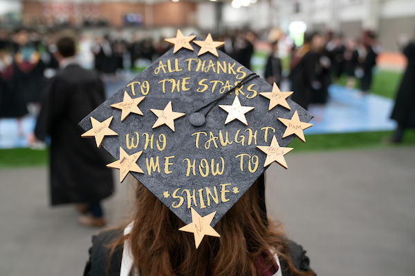 Student wearing graduation cap decorated with gold stars reading All thanks to the stars who taught me how to shine