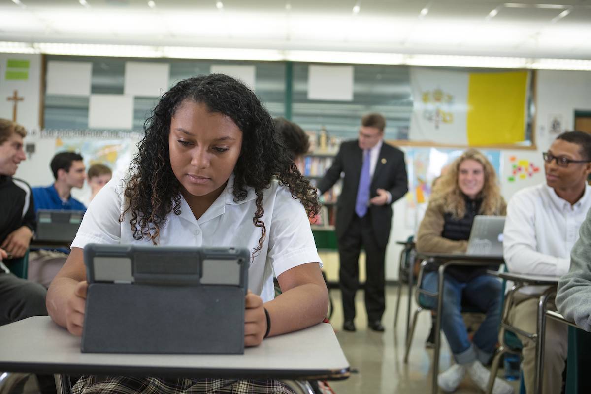 Student in high school uniform in a classroom. A professor and other students work in the background