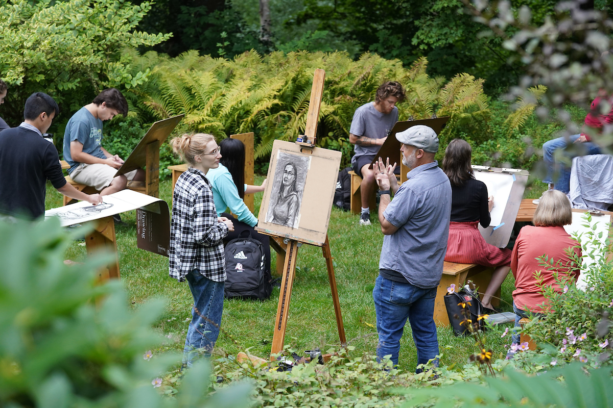 students with easles work on art outside in green grassy area