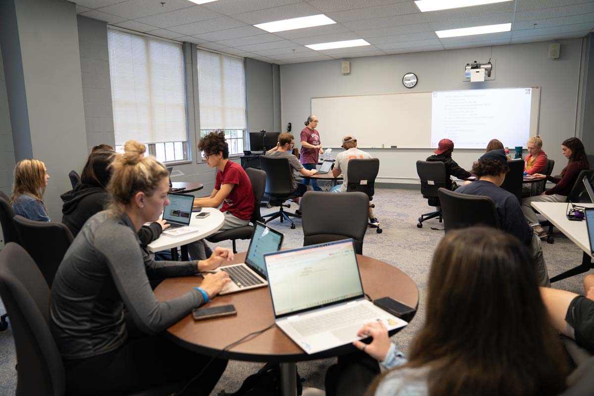 Classroom with several tables and students working on their computers