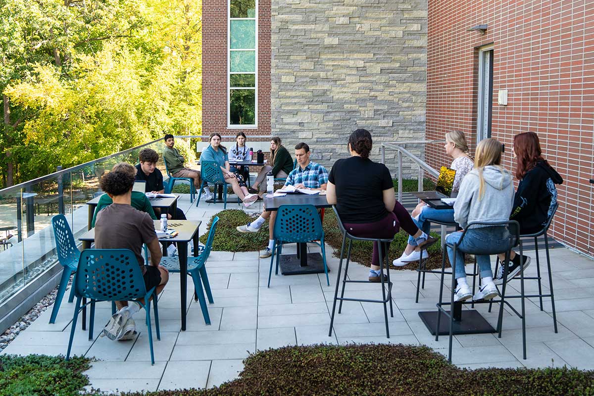 tudents and professor holding class on the green balcony of the Science Building which overlooks campus