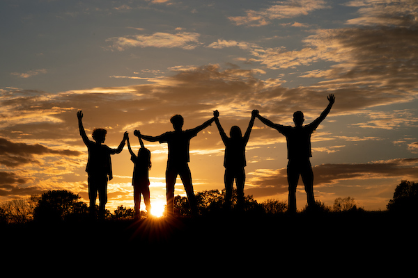 family backlit by sunset, with arms in the air