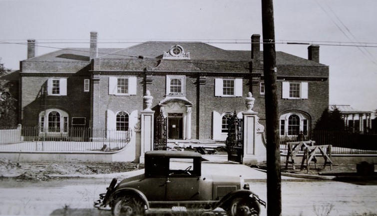 Old black and white photo of Brookby with an early automobile out front. Two floors with windows and a grand gate in front.
