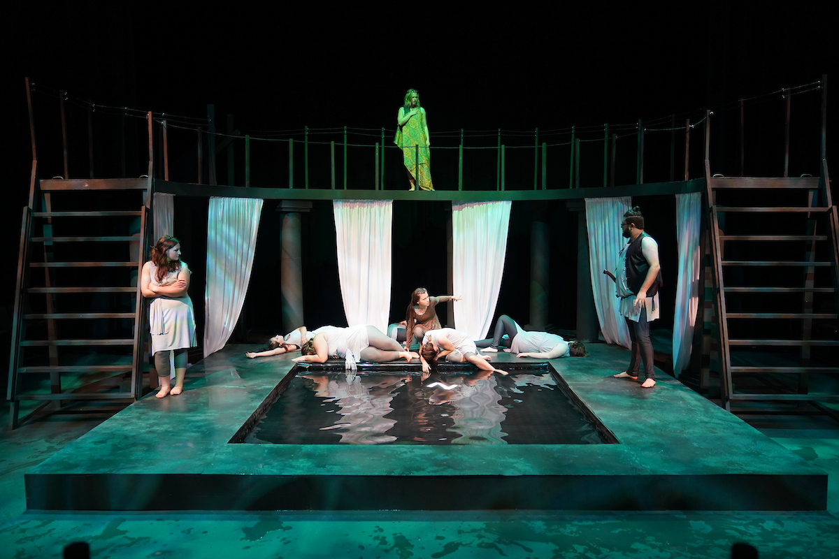 Students performing on stage with a courtyard like structure featuring a pool of water at the center