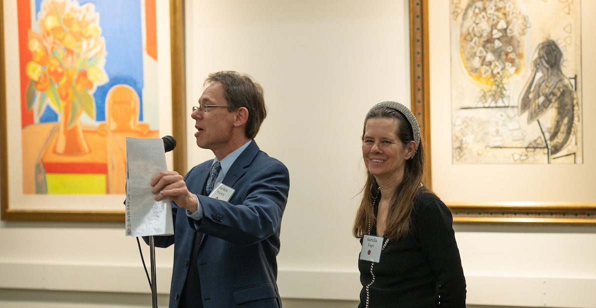 Aurelia Engel, daughter of Francoise Gilot stands beside Jochen Wierech who speaks into a microphone in the gallery with Gilot works behind him.