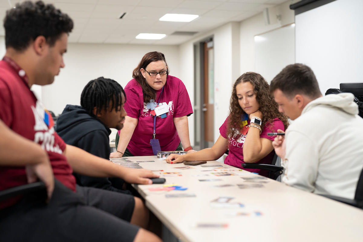 Students and a professor look at cards on a table intently