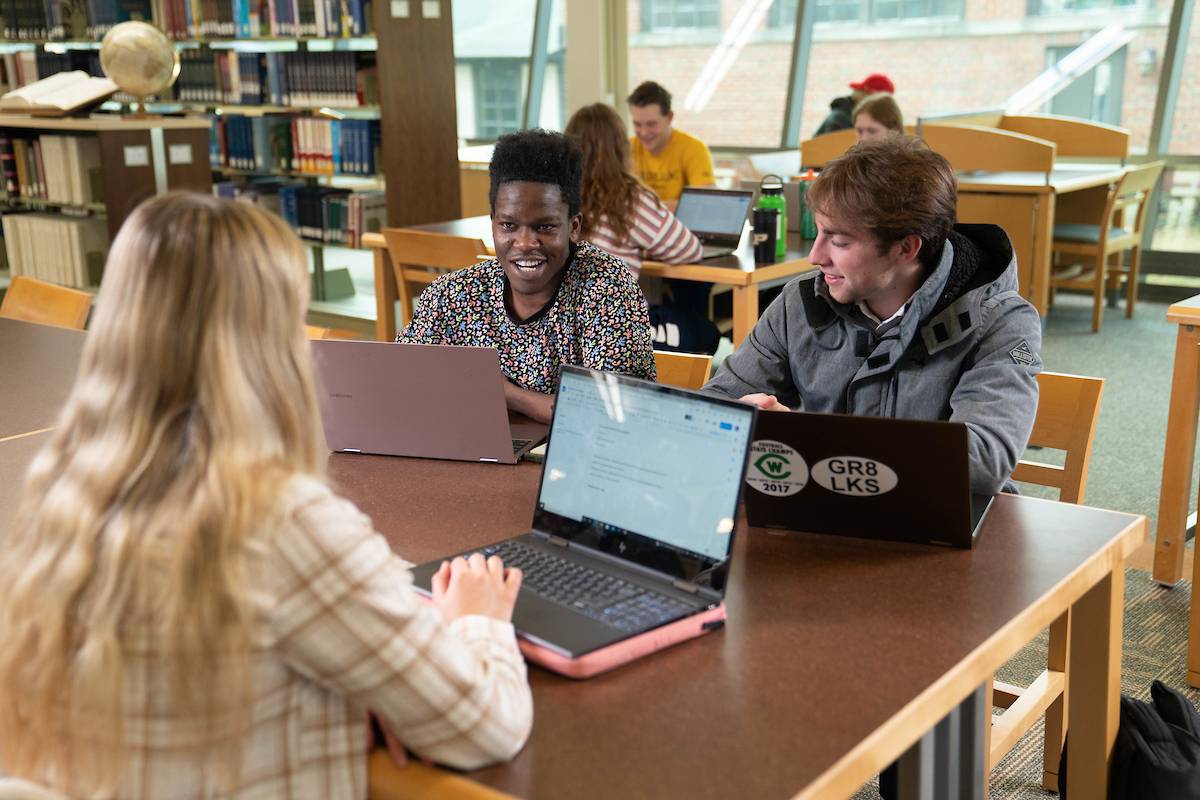 Students talking at a table with laptops open