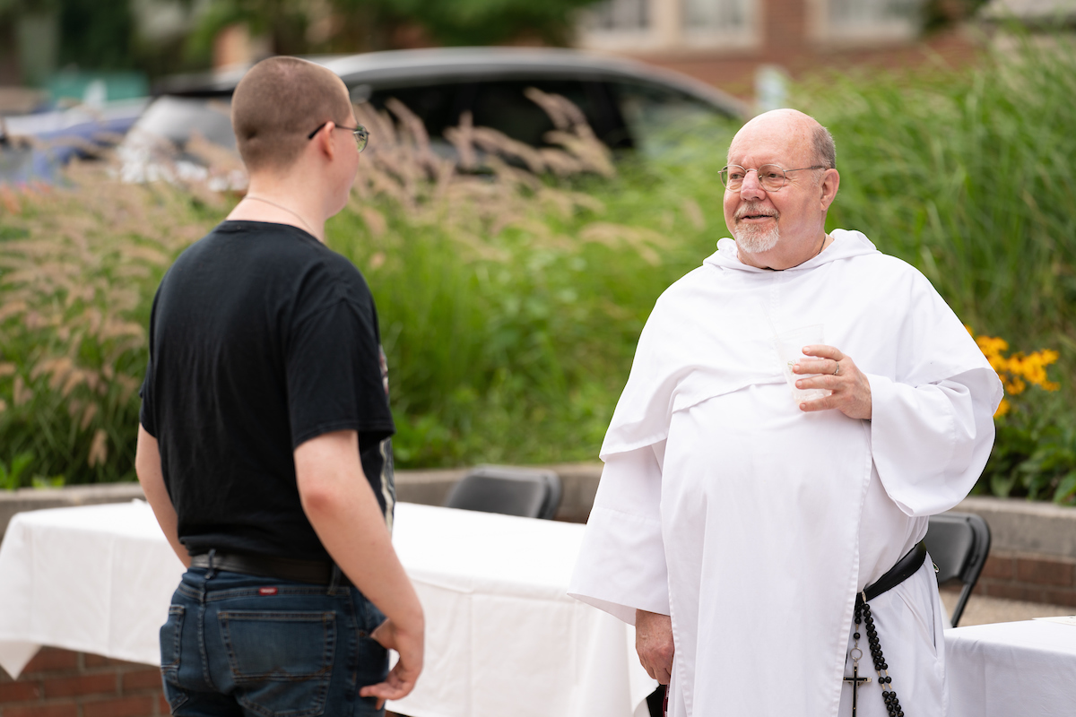 Father Stan in his white robes speaks to a student outside