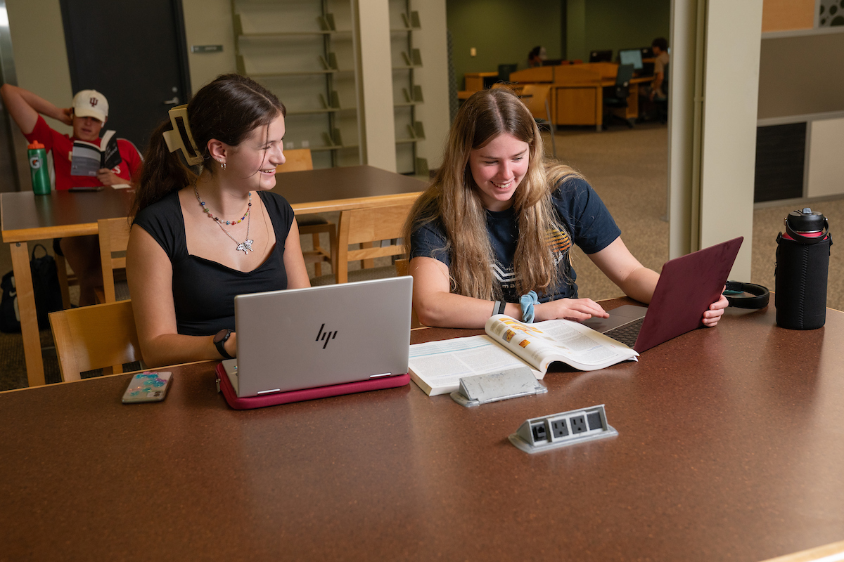Two students smiling and talking with laptops and books
