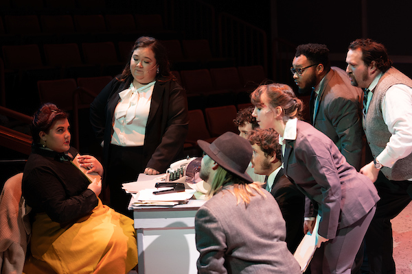 Students performing in 9 to 5, gathered around someone at a desk
