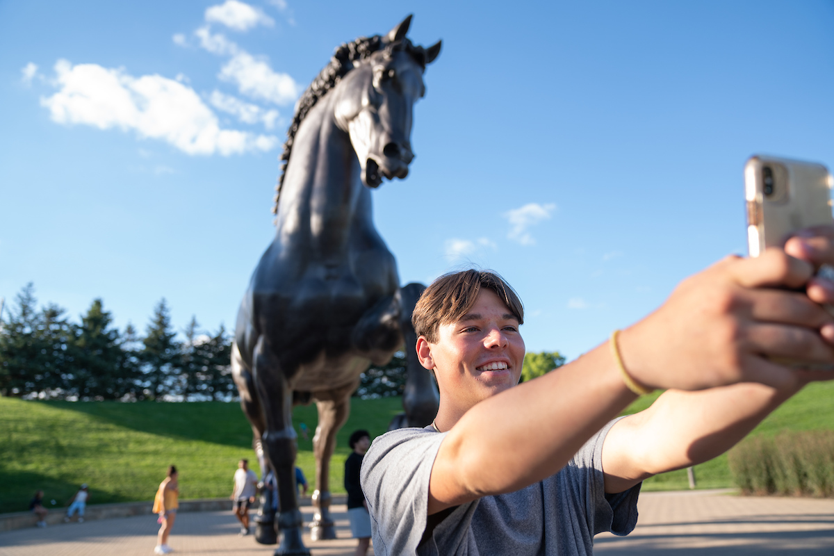 student taking a selfie with 2 story tall horse statue