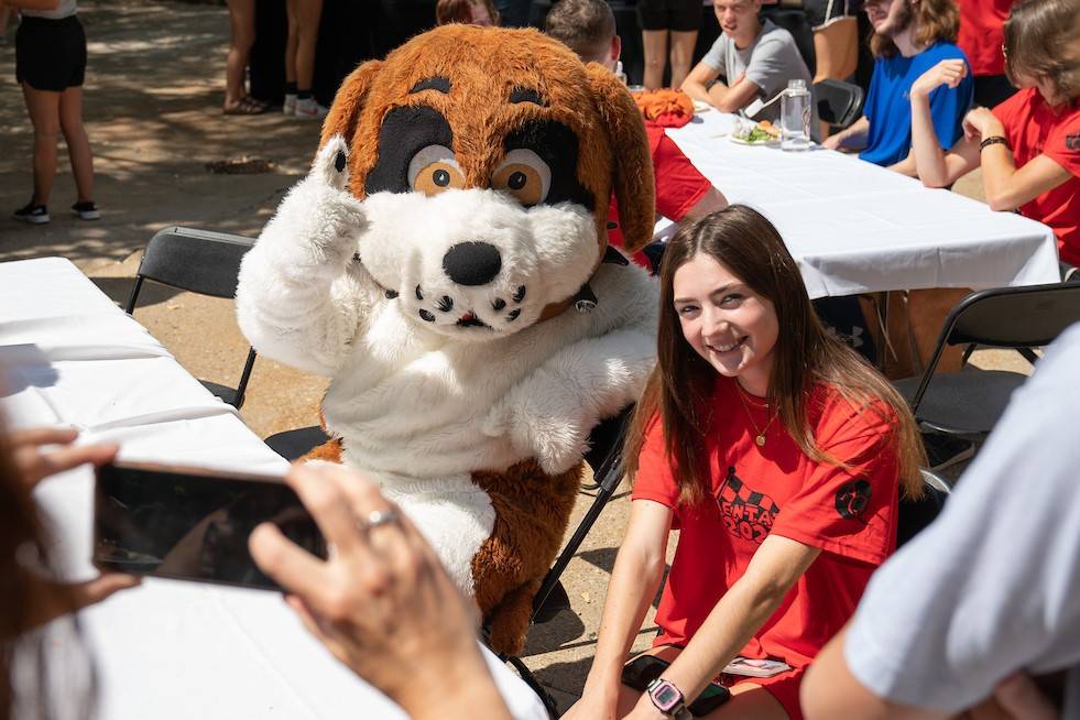 Student posing beside Saint Bernard Mascot Nelson who gives a thumbs up