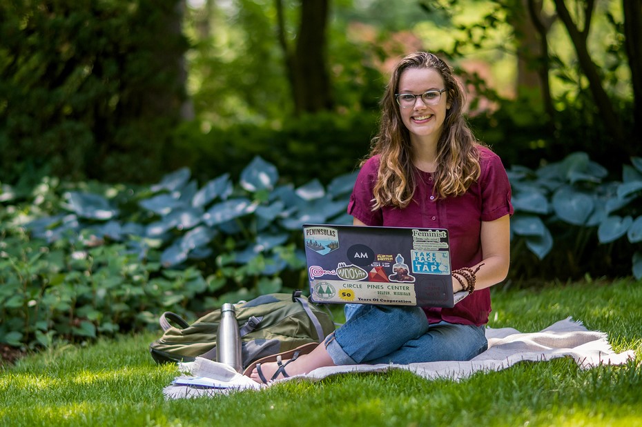 Student sitting on blanket on lawn with laptop smiling