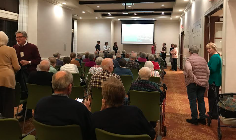 Residents fill rows of seats at a presentation by Aquinas students who stand in front of a projector screen