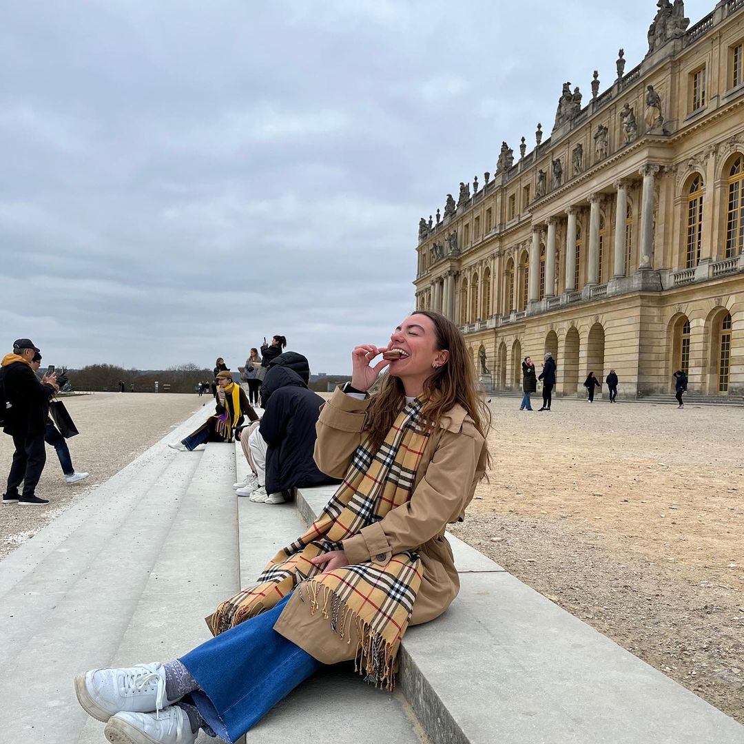 Student eating a macaron on the steps of a castle or palace.